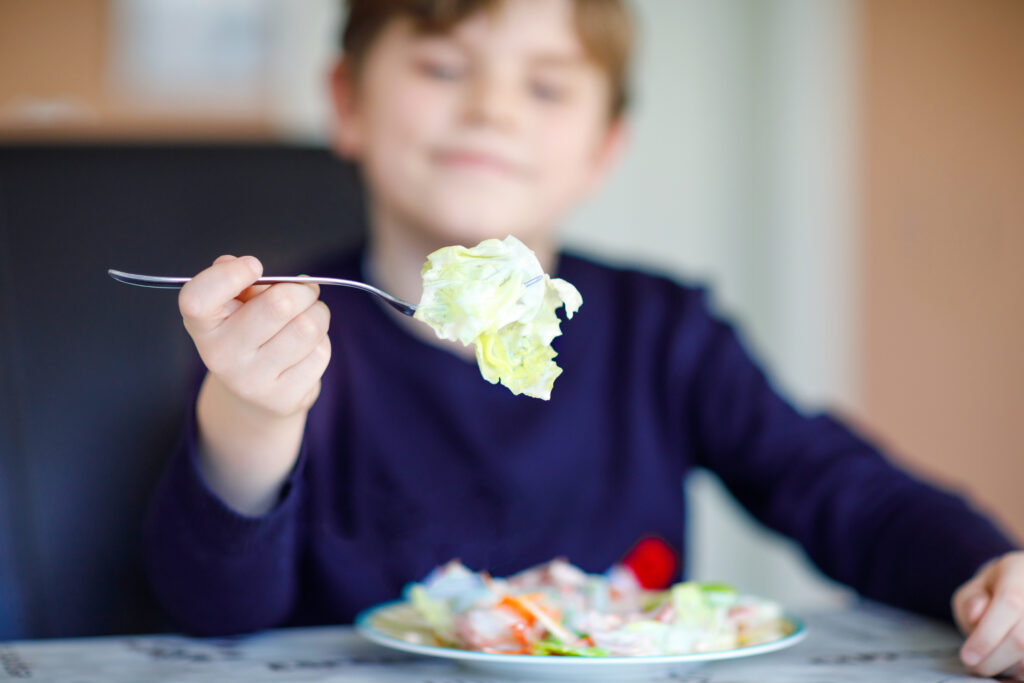 En pojke håller upp en gaffel med mat framför sig. Foto.