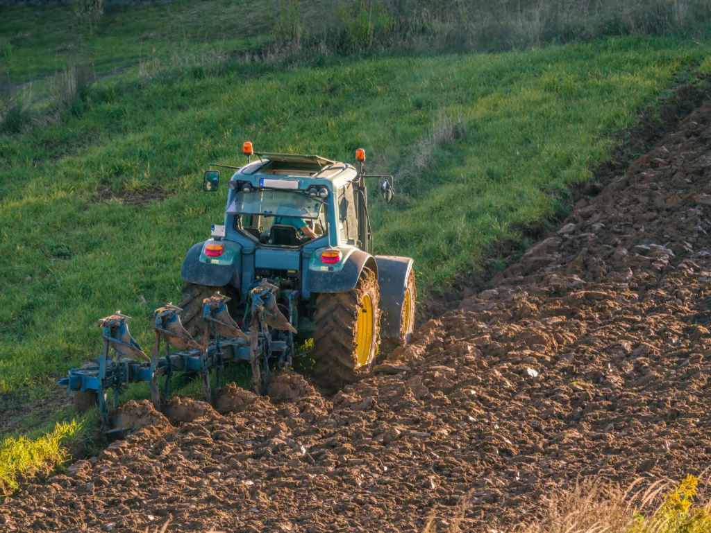 Traktor som plöjer ett fält i solnedgången.